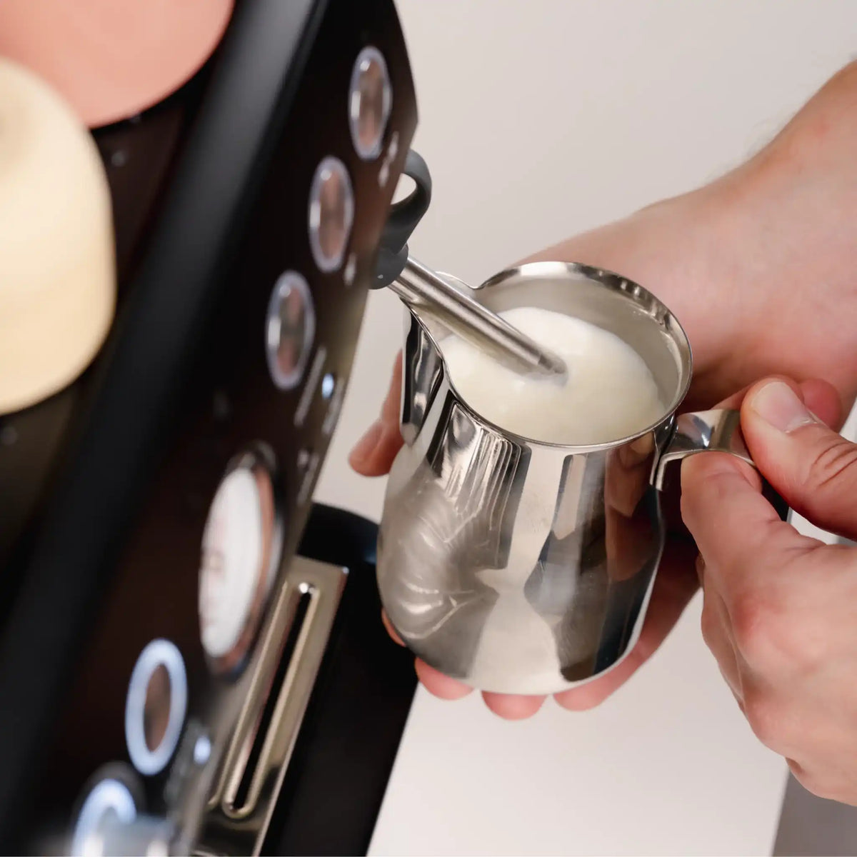 Melkkannetje met opschuimende melk onder stoompijp van espressomachine tijdens bereiding door thuisbarista