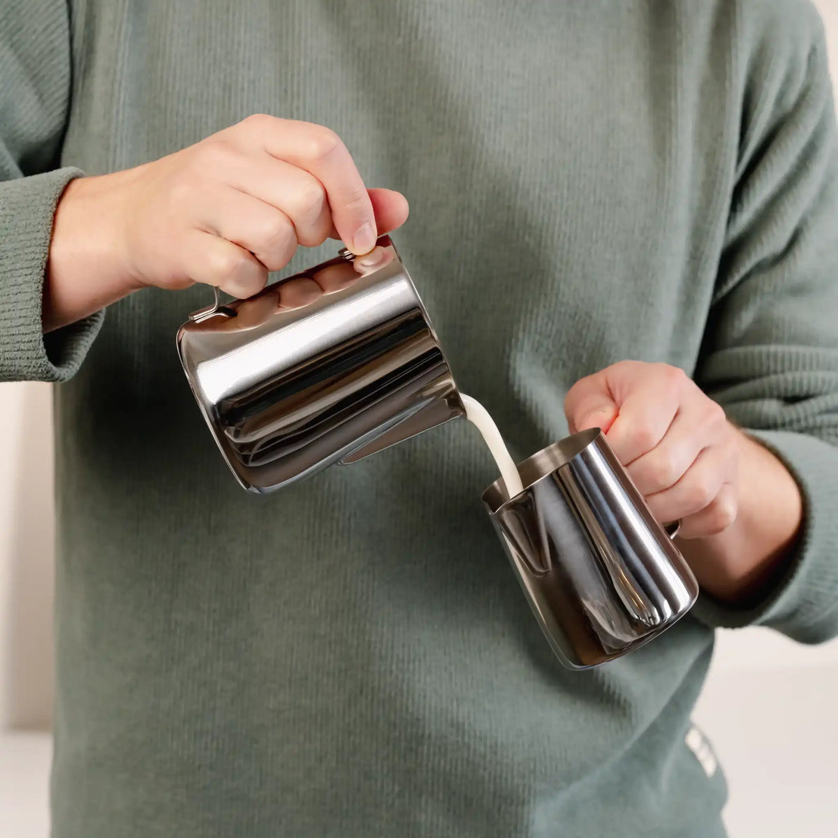 Thuisbarista giet opgeschuimde melk over tussen twee melkkannetjes voor betere textuur en controle bij latte art