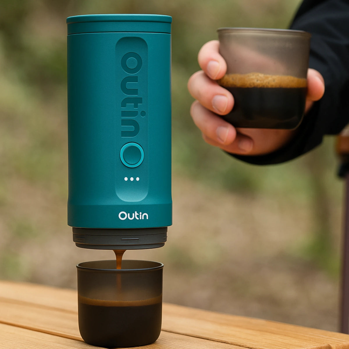 Draagbare OutIn Nano espressomachine met versgemalen koffie op houten tafel in een bosrijke omgeving.