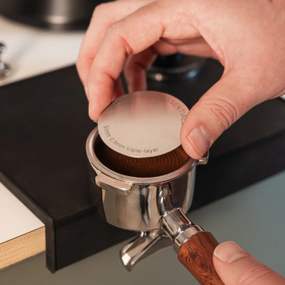 Hand legt een 51 mm puck screen op de koffie in een filterdrager