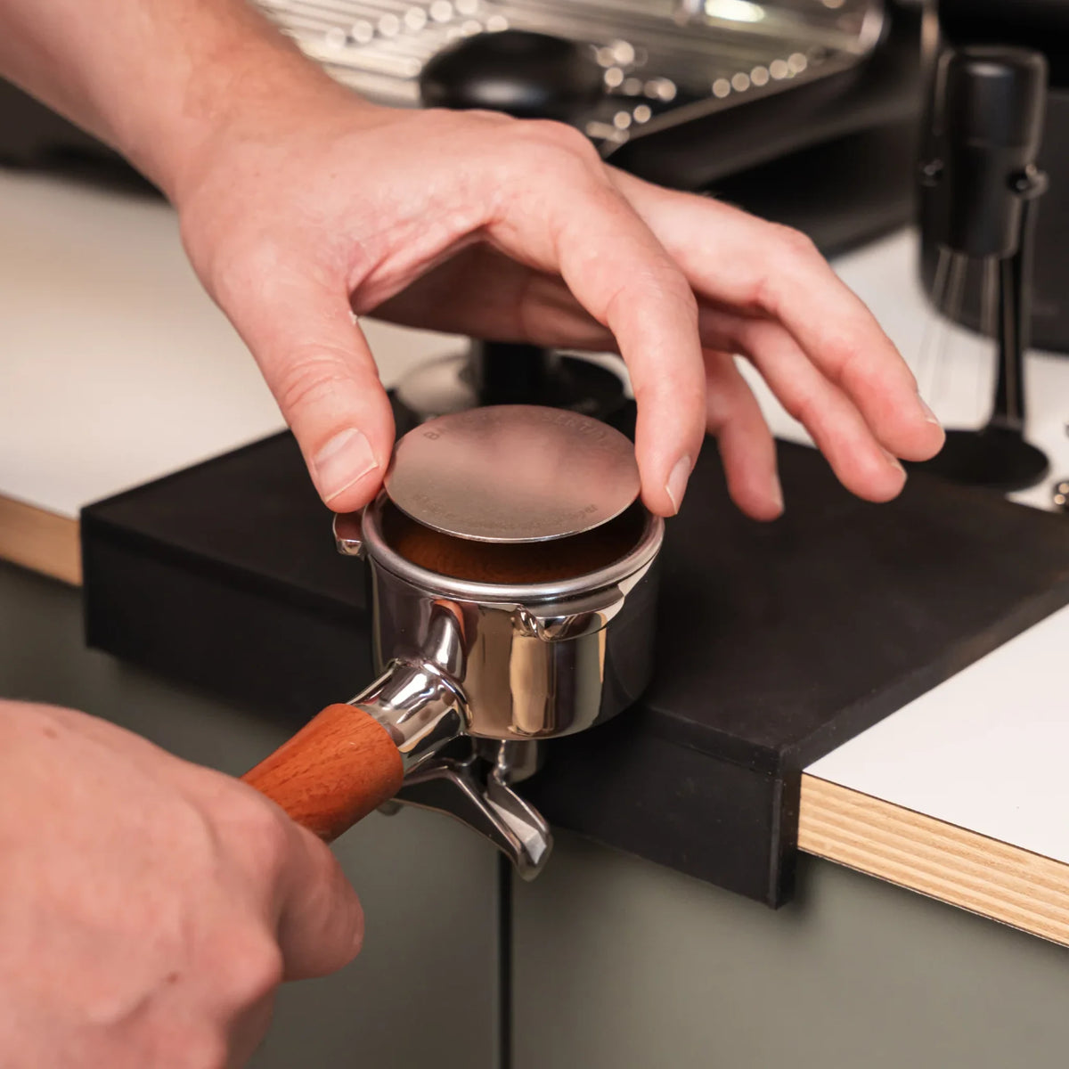 Hand legt een 53,3 mm puck screen op de koffie in een filterdrager