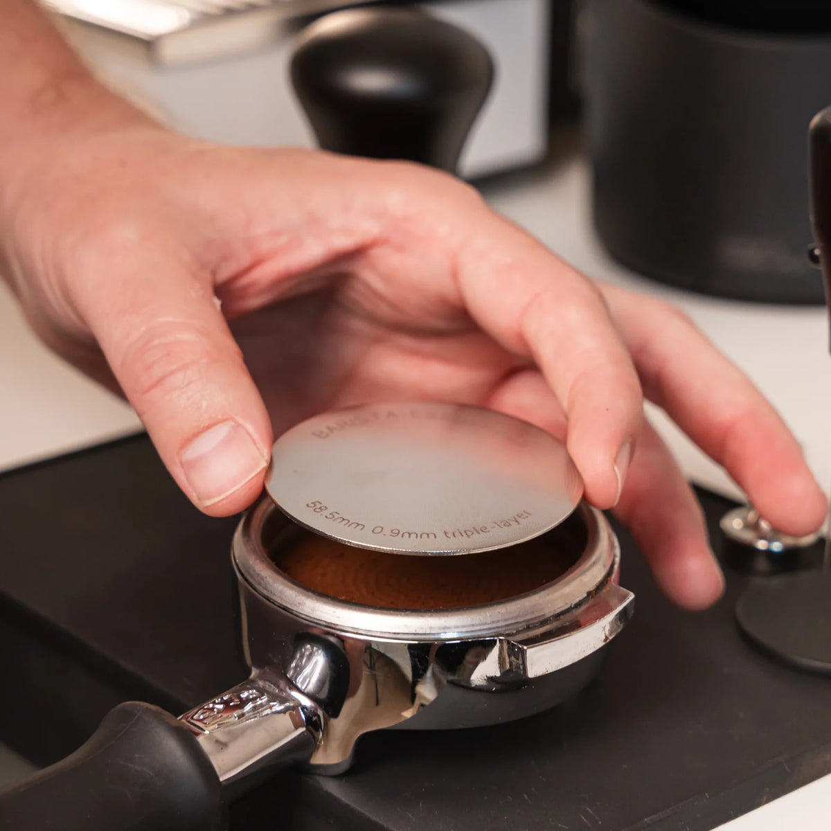 Hand legt een 58,5 mm puck screen op de koffie in een filterdrager