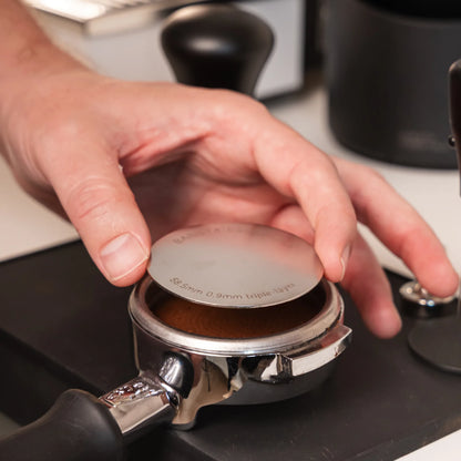 Hand legt een 58,5 mm puck screen op de koffie in een filterdrager