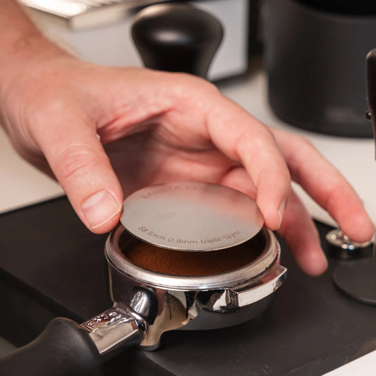 Hand legt een 58,5 mm puck screen op de koffie in een filterdrager