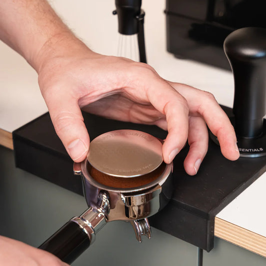 Hand legt een 58 mm puck screen op de koffie in een filterdrager