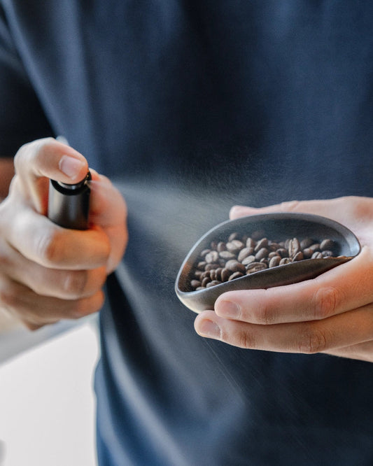 Een fijne nevel uit de RDT Spray boven koffiebonen in een doseerbakje
