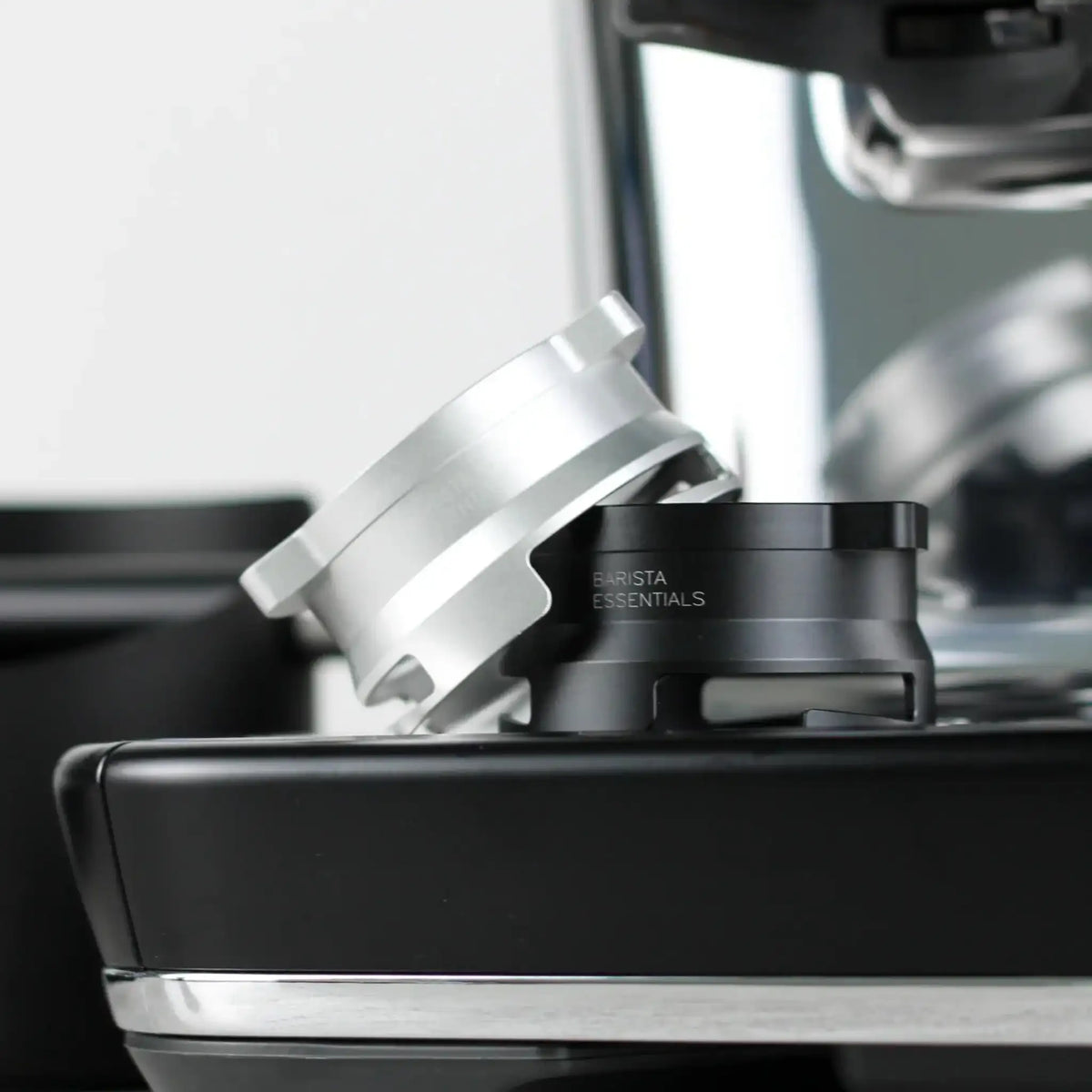Zwarte en zilveren doseerring naast elkaar op de lekbak van een espressomachine