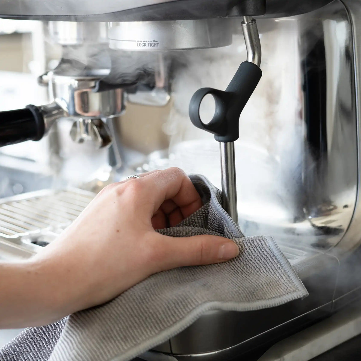 Hand van thuisbarista reinigt stoompijp van espressomachine met barista doekje na het melk opschuimen