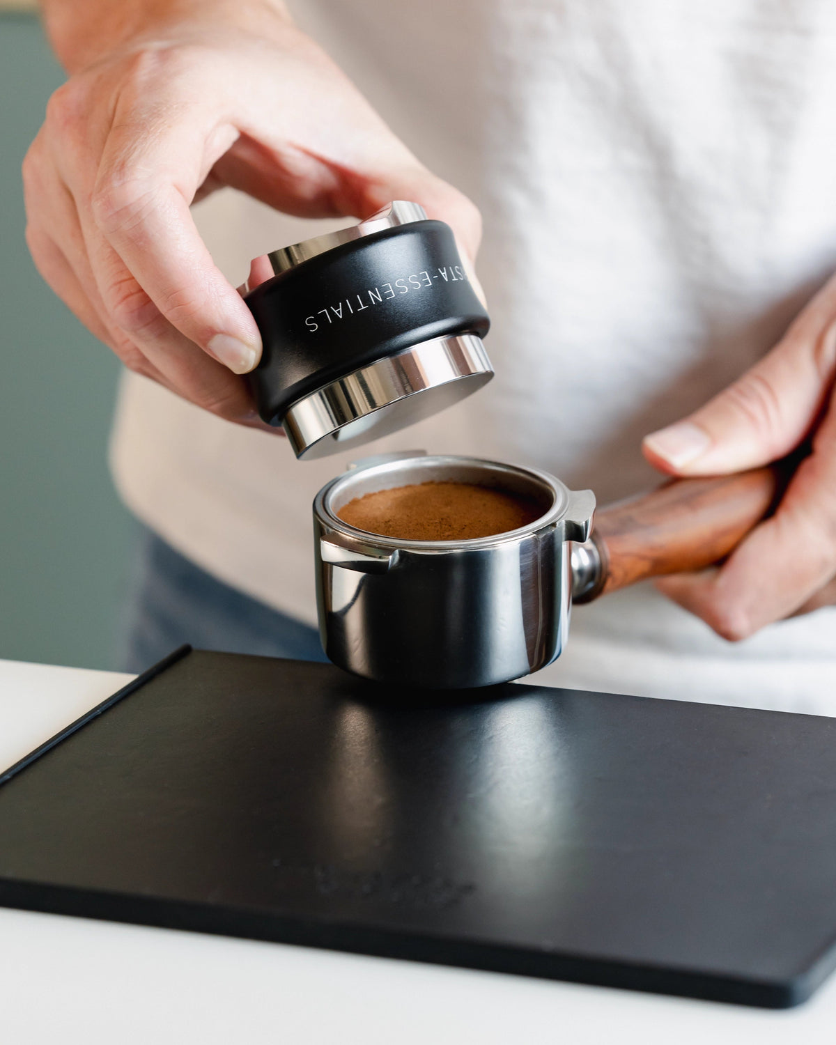 Zwarte tamper en verdeler boven een vlak getampte koffiepuck
