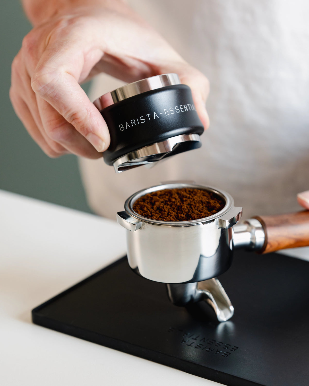 Zwarte tamper en verdeler boven een filterbakje met losse gemalen koffie