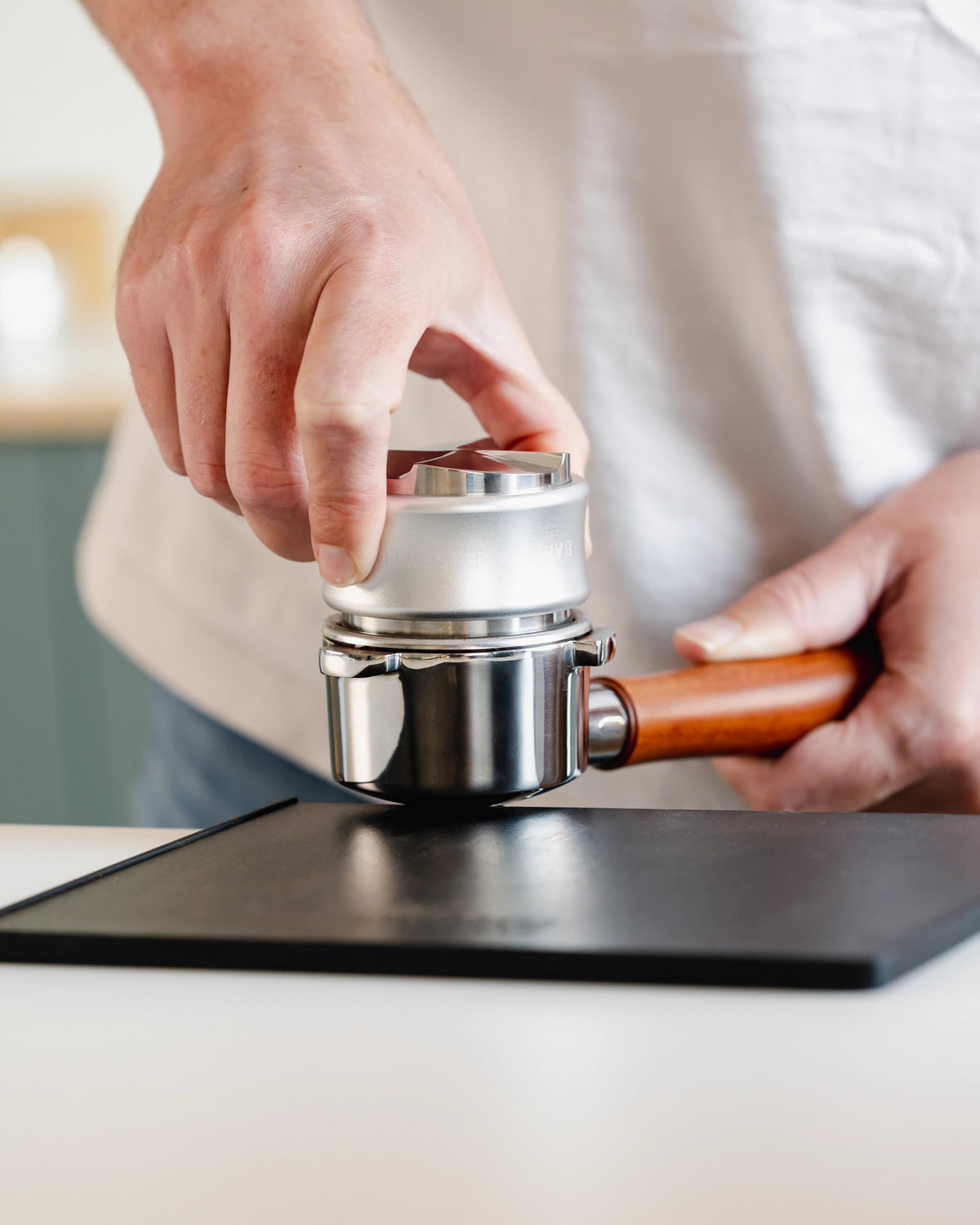 Zilverkleurige tamper en verdeler tijdens het tampen op een portafilter