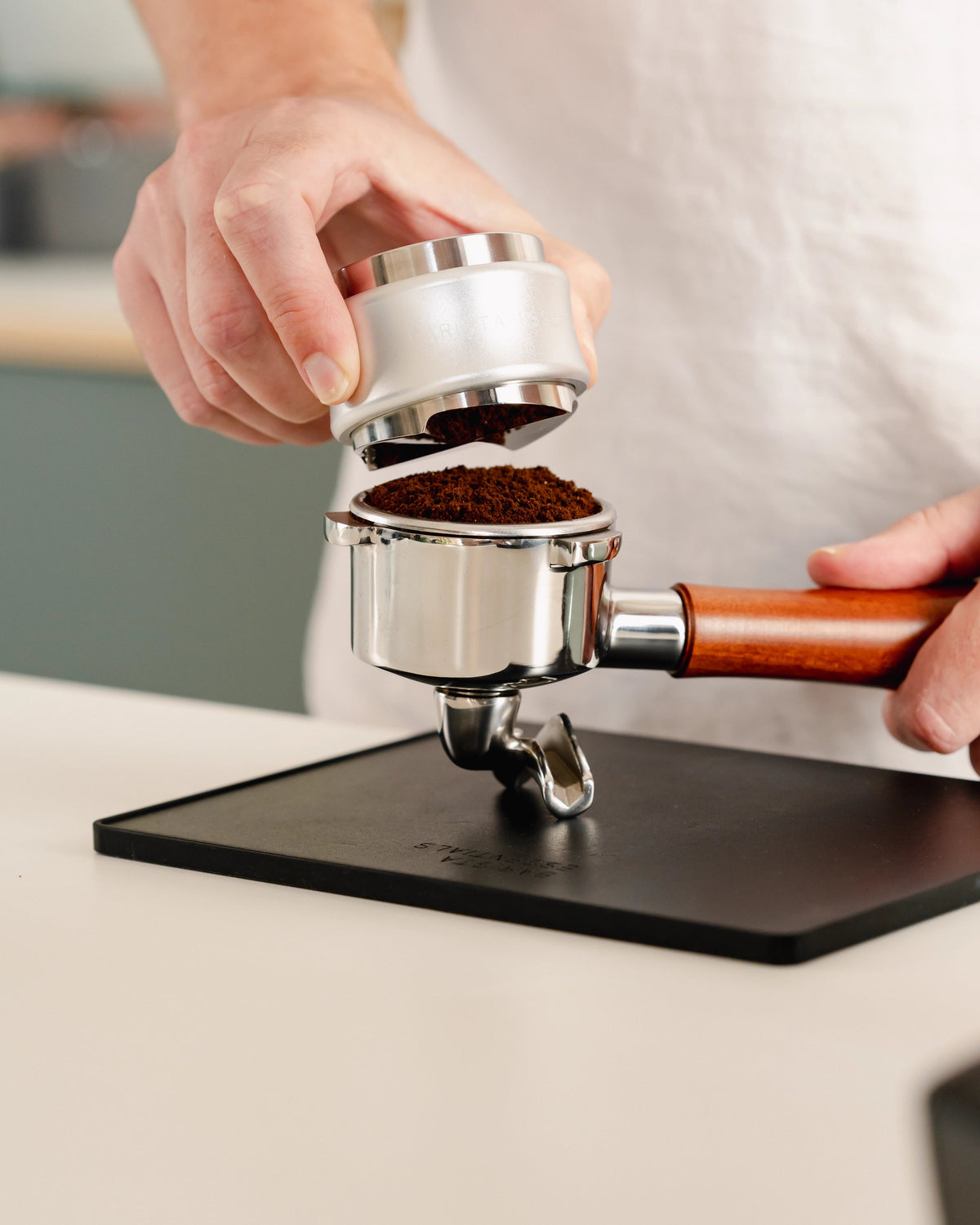 Zilverkleurige tamper en verdeler boven een filterbakje met losse gemalen koffie