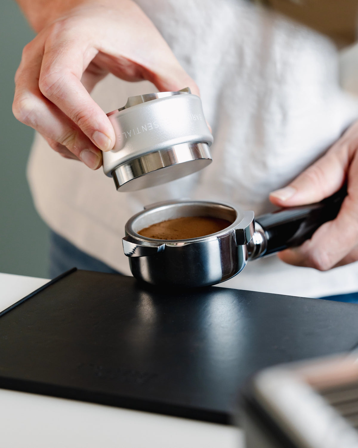 Zilverkleurige tamper en verdeler boven een vlak getampte koffiepuck