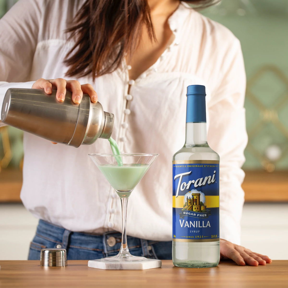 Vrouw maakt een stijlvolle cocktail met Torani suikervrije vanillesiroop – perfect voor bewuste genieters die houden van creatieve, suikervrije drankjes