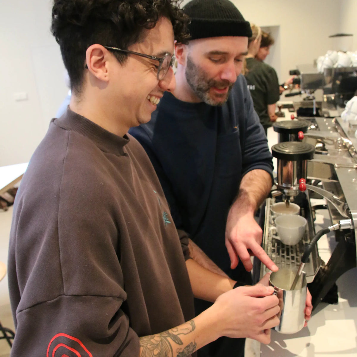Barista-trainer helpt een deelnemer met het opschuimen van melk voor een cappuccino.