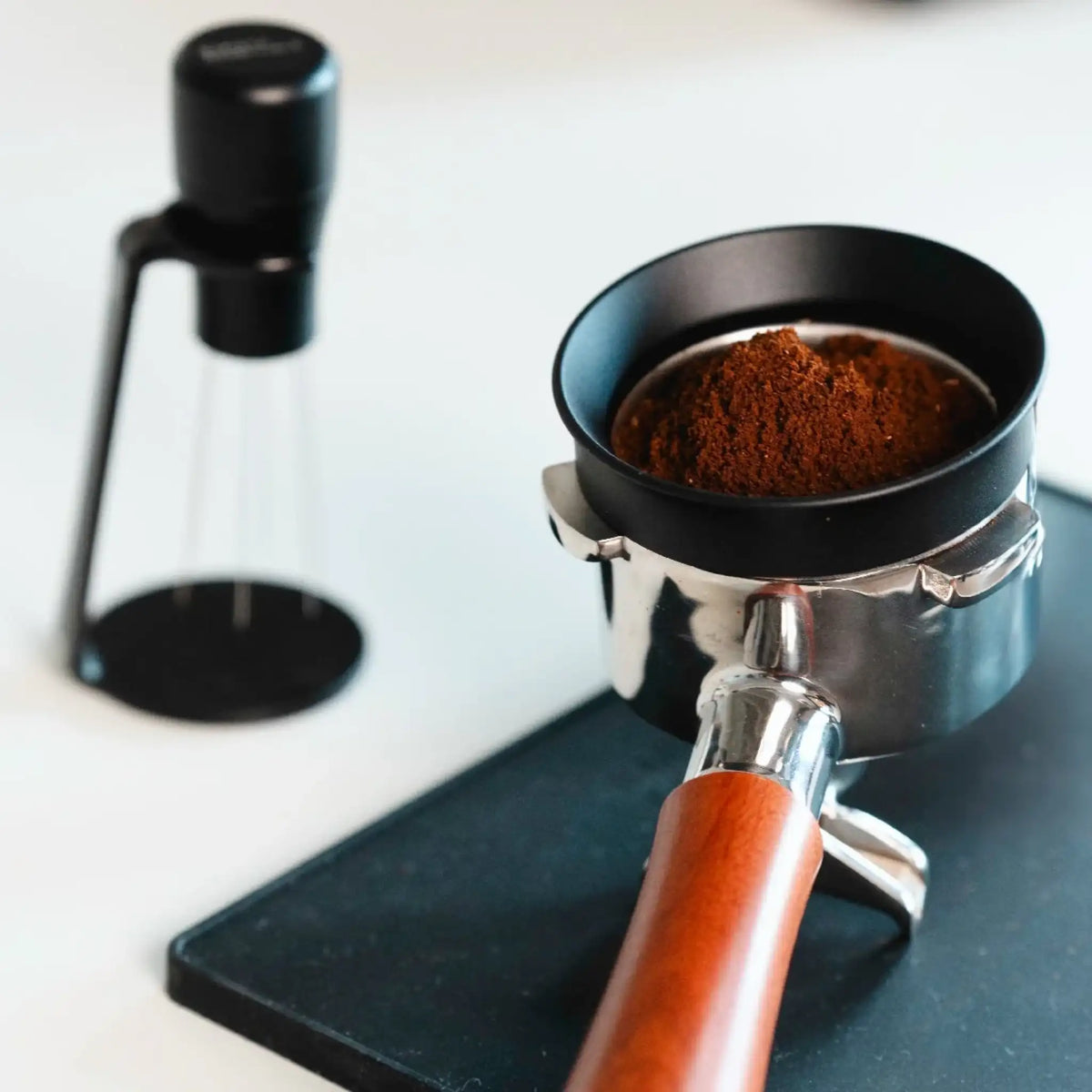 Zwarte WDT-tool met houder naast een filterdrager met koffie