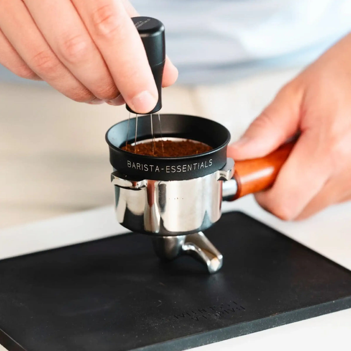 Hand roert met een zwarte WDT-tool door koffie in een filterbakje