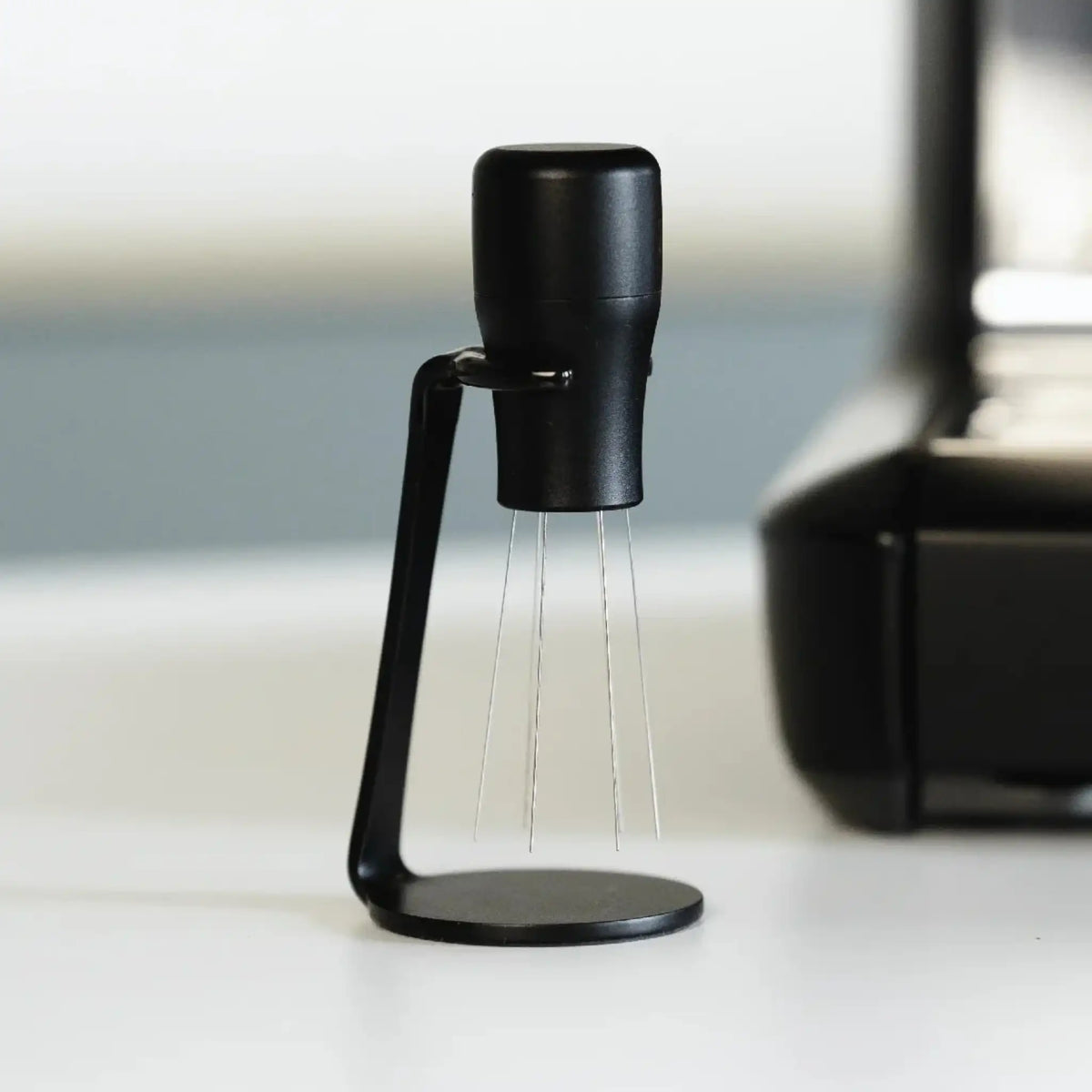 Zwarte WDT-tool met houder naast een espressomachine