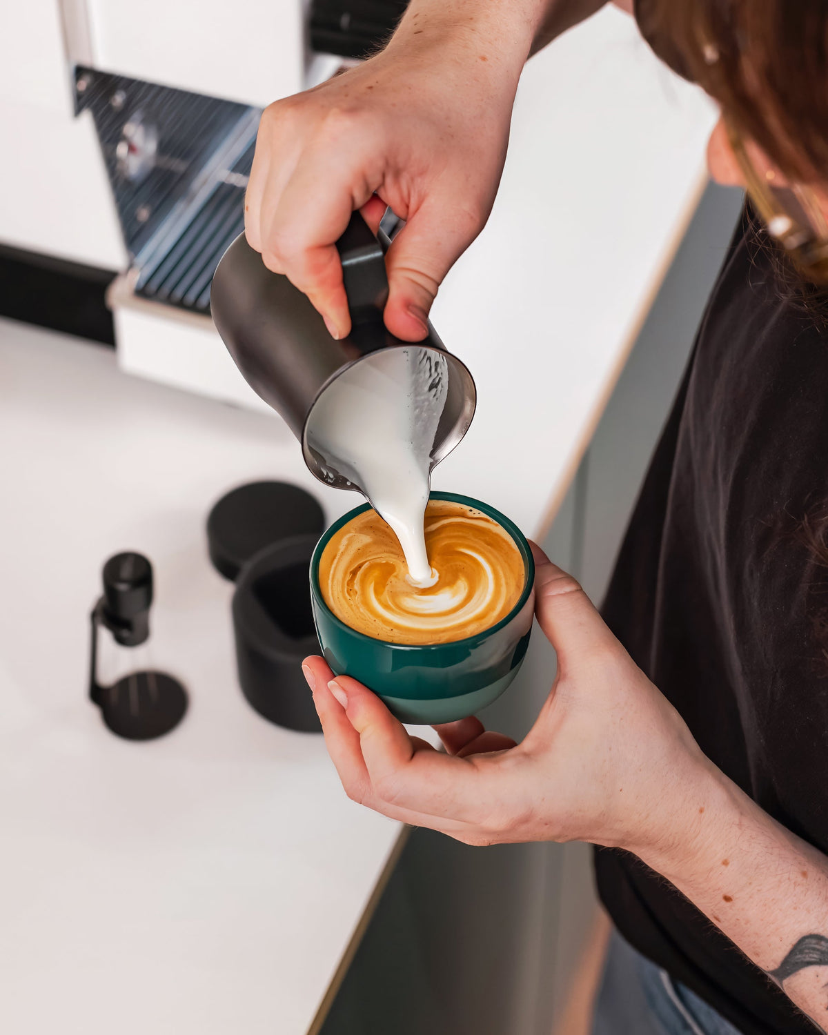 Melk wordt uit een zwarte Italiaanse melkkan 350 ml in een kop koffie geschonken