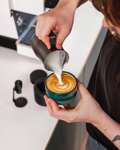Melk wordt uit een zwarte Italiaanse melkkan 350 ml in een kop koffie geschonken