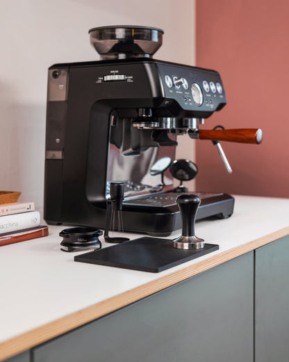 Zwarte tamper op een tampingmat naast een Sage espressomachine