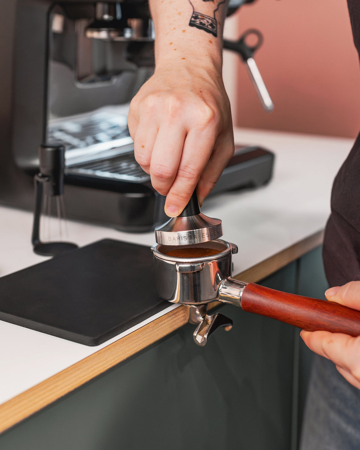 Hand drukt koffie aan met een zwarte tamper in een filterdrager