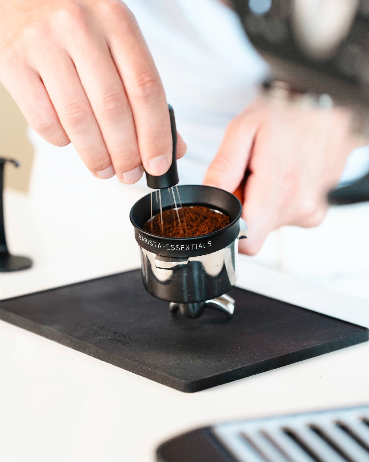 Zwarte WDT-tool roert door gemalen koffie in een filterbakje met doseerring